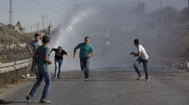 Palestinians run as Israeli troops use a water canon to disperse protesters during clashes in Jalazoun refugee camp, near the West Bank city of Ramallah (AP photo)